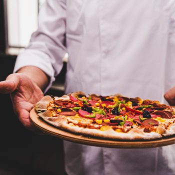 chef-holding-wooden-plate-with-delicious-pizza-it-kitchen