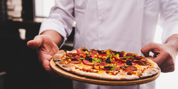 chef-holding-wooden-plate-with-delicious-pizza-it-kitchen